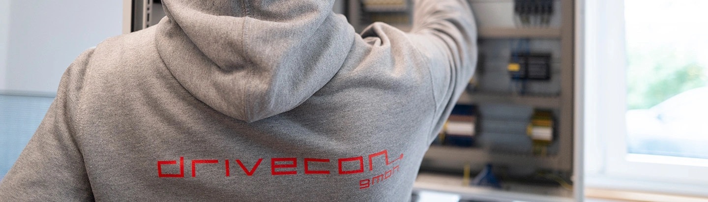 Back view of a hoodie with DriveCon logo, the employee is standing in front of a control cabinet